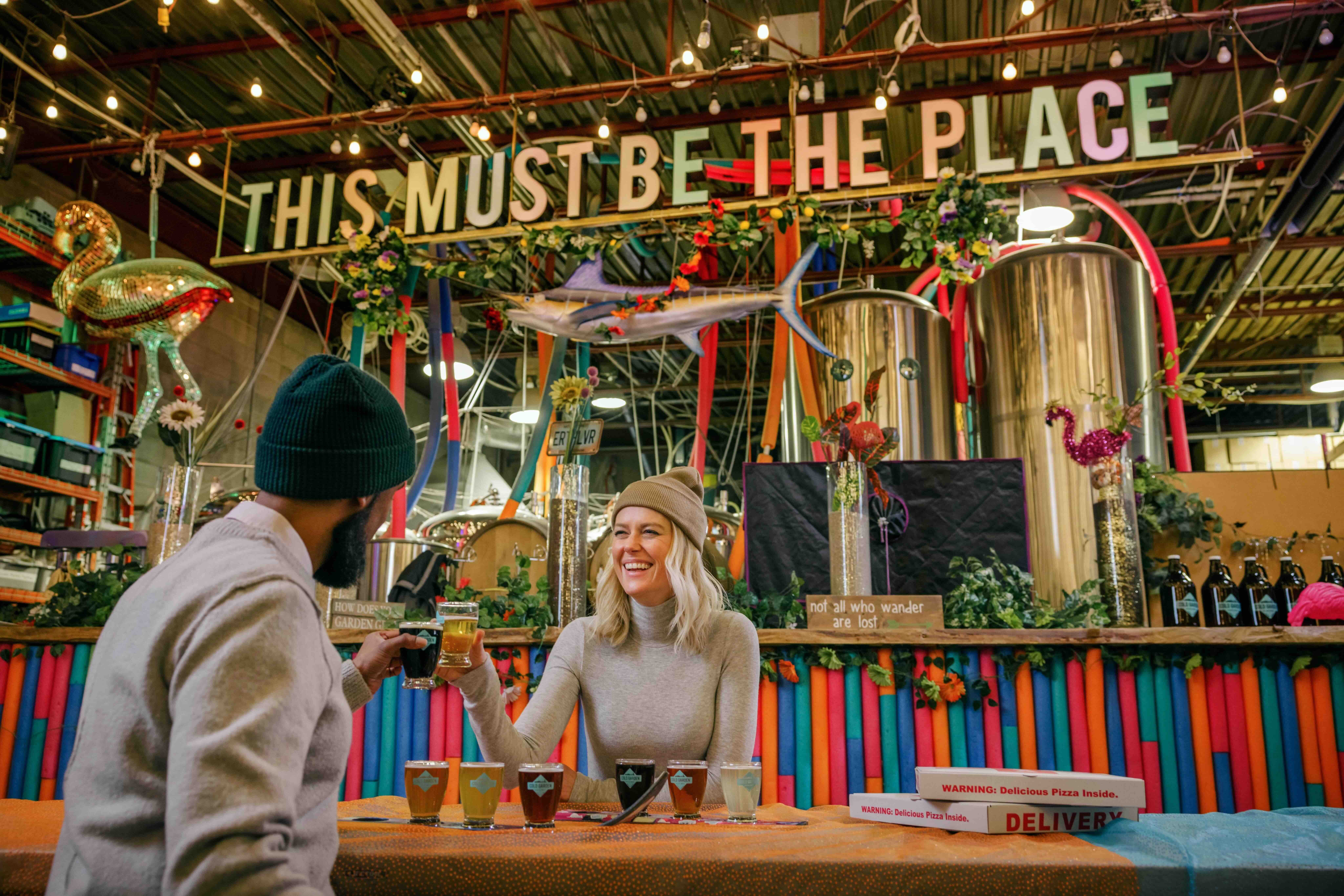 Two people sit at a table in Cold Garden toasting with a flight of beers.